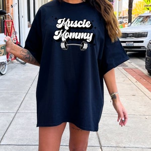 May include: A black oversized t-shirt with a white graphic that says "Muscle Mommy" with a barbell underneath the text.