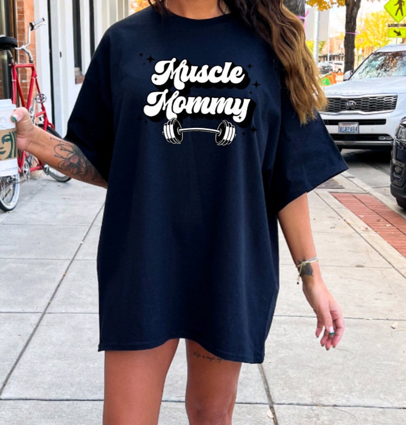 May include: A black oversized t-shirt with a white graphic that says "Muscle Mommy" with a barbell underneath the text.
