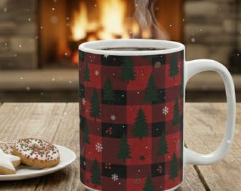 May include: A white ceramic mug with a red and black plaid pattern featuring green Christmas trees and snowflakes. The mug is filled with a dark liquid and is steaming. A plate of cookies sits nearby.