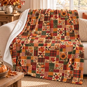 May include: A plush throw blanket featuring a patchwork design of autumn-themed squares. The pattern includes illustrations of pumpkins, sunflowers, maple leaves, acorns, pinecones, and mushrooms in shades of orange, red, green, and brown.