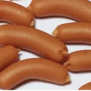 Könnte beinhalten: Eine Gruppe kleiner, brauner, wurstförmiger Snacks. Die Snacks sind in einem zufälligen Muster auf einer weißen Oberfläche angeordnet.