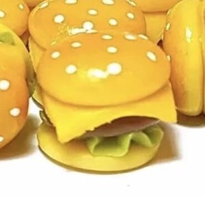 May include: A group of miniature yellow and brown toy hamburgers with white sesame seeds on top. The hamburgers are made of polymer clay and are about the size of a dime.