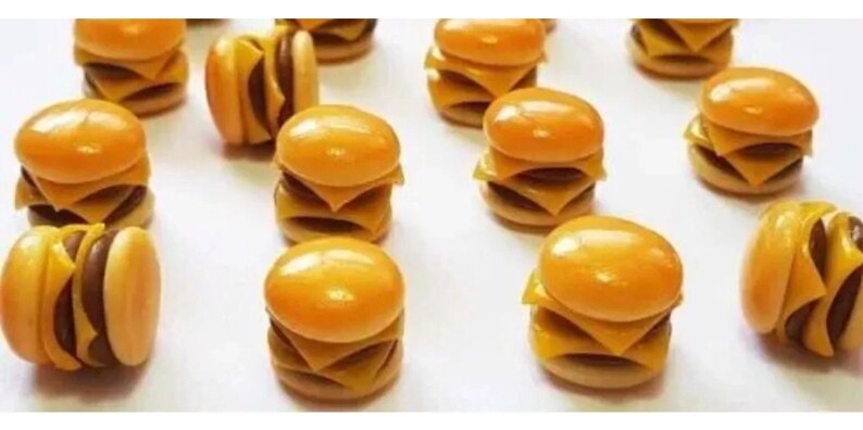 May include: A collection of miniature, yellow and brown, double-decker cheeseburger-shaped polymer clay charms.