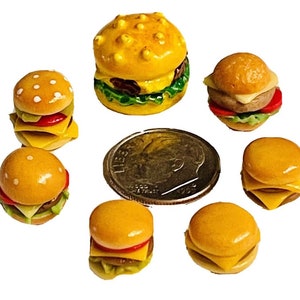 May include: A collection of seven miniature toy hamburgers, each with a sesame seed bun, cheese, lettuce, and tomato. The hamburgers are arranged on a white background.