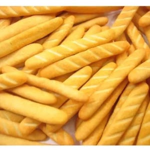 May include: A close-up of a pile of thin, crispy, golden brown breadsticks. The breadsticks are arranged in a random pattern, with some overlapping.