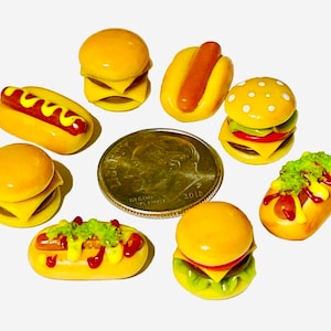 May include: A collection of miniature food items, including hamburgers, hot dogs, and french fries, made of polymer clay. The items are painted in realistic colors and have detailed textures.