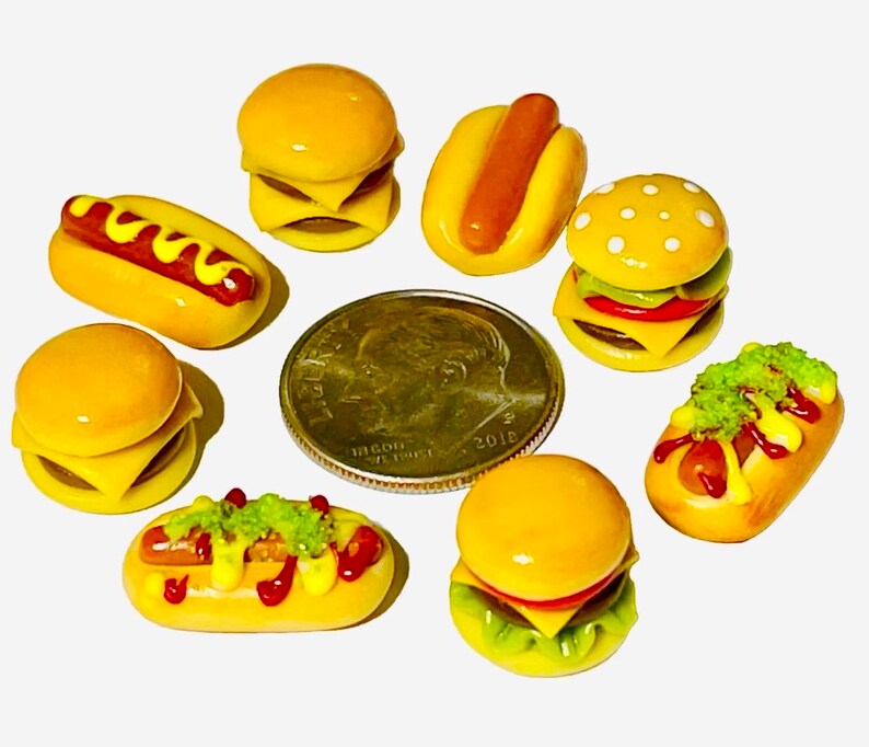 May include: A collection of miniature food items, including hamburgers, hot dogs, and french fries, made of polymer clay. The items are painted in realistic colors and have detailed textures.