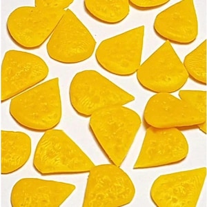 May include: A collection of bright yellow, wedge-shaped candies, possibly cheese-flavored, arranged on a white surface. The candies have a textured surface and a slightly irregular shape, suggesting a homemade or artisanal quality.