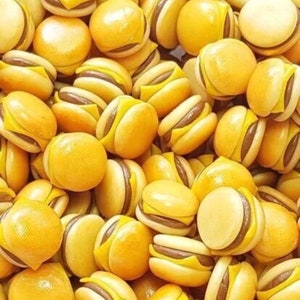 May include: A large group of miniature yellow and brown hamburger shaped charms. The charms are made of a smooth, shiny material.