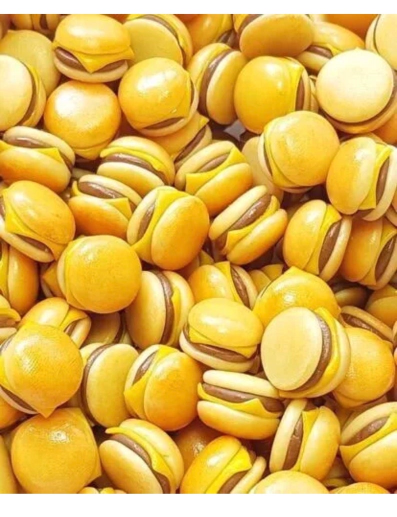 May include: A large group of miniature yellow and brown hamburger shaped charms. The charms are made of a smooth, shiny material.