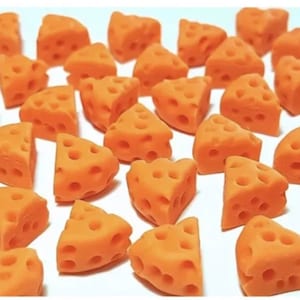Op de afbeelding: Een verzameling kleine, oranje, driehoekige kaaswiggen met gaten. De kaaswiggen zijn willekeurig gerangschikt op een wit oppervlak.