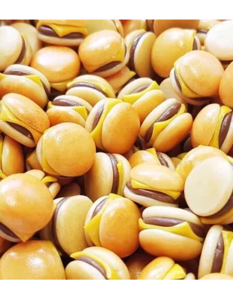 May include: A close-up of a pile of miniature, yellow, and brown hamburger-shaped charms. The charms are made of polymer clay and have a realistic appearance.