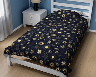 以下が含まれることがあります： 濃い青色の背景に、金色の星、月、太陽が繰り返し描かれた、ツインサイズのベッドスプレッドです。