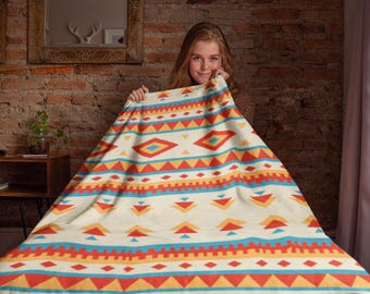 May include: A white throw blanket with a colorful geometric pattern in shades of red, orange, yellow, and blue. The pattern features triangles, diamonds, and stripes.