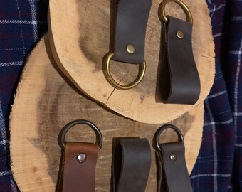 May include: Three leather key fobs with metal rings. The fobs are brown, dark brown, and black. The rings are gold and silver.