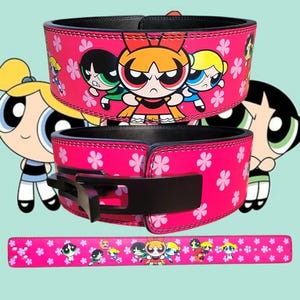 May include: Pink weightlifting belt with a black buckle and a pattern of pink flowers and the Powerpuff Girls characters. The belt is made of leather and has a stitched edge.