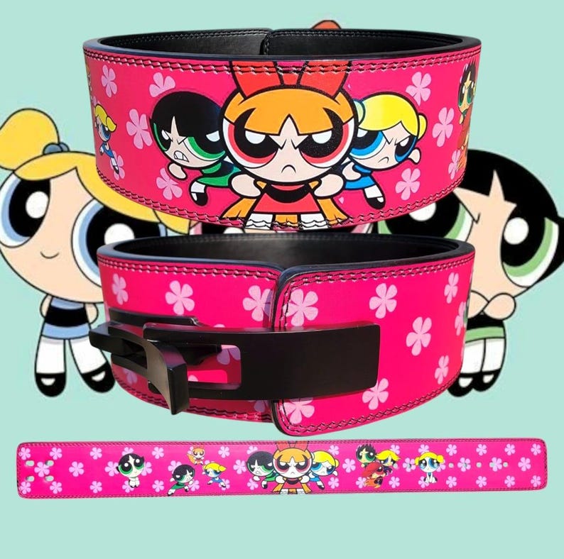 Peut inclure: Ceinture de musculation rose avec une boucle noire et un motif de fleurs roses et les personnages de Powerpuff Girls. La ceinture est en cuir et a un bord cousu.