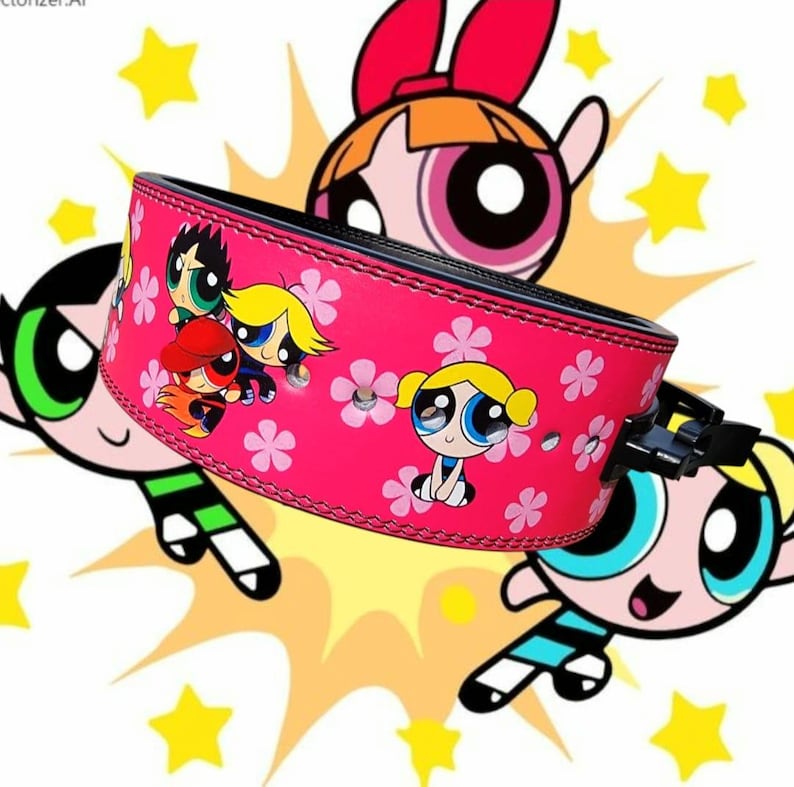 Peut inclure: Ceinture de musculation rose avec une boucle noire et un motif de dessin anim&eacute; color&eacute; repr&eacute;sentant les Powerpuff Girls. La ceinture a un fond rose avec des fleurs blanches et les Powerpuff Girls sont au centre de la ceinture.