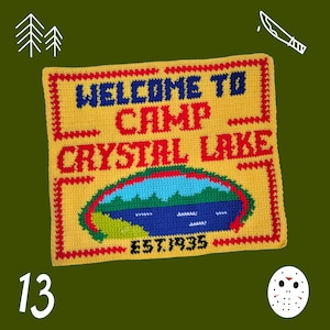 May include: Yellow crocheted sign with red trim that reads "Welcome to Camp Crystal Lake Est. 1935". The sign features a blue lake with green trees and a white border.
