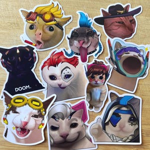 Peut inclure: Une collection d'autocollants de chats colorés avec divers designs. Les autocollants présentent des chats avec différentes expressions et accessoires, tels que des lunettes, des chapeaux et des cheveux bleus. Certains autocollants ont du texte comme "DOOM."