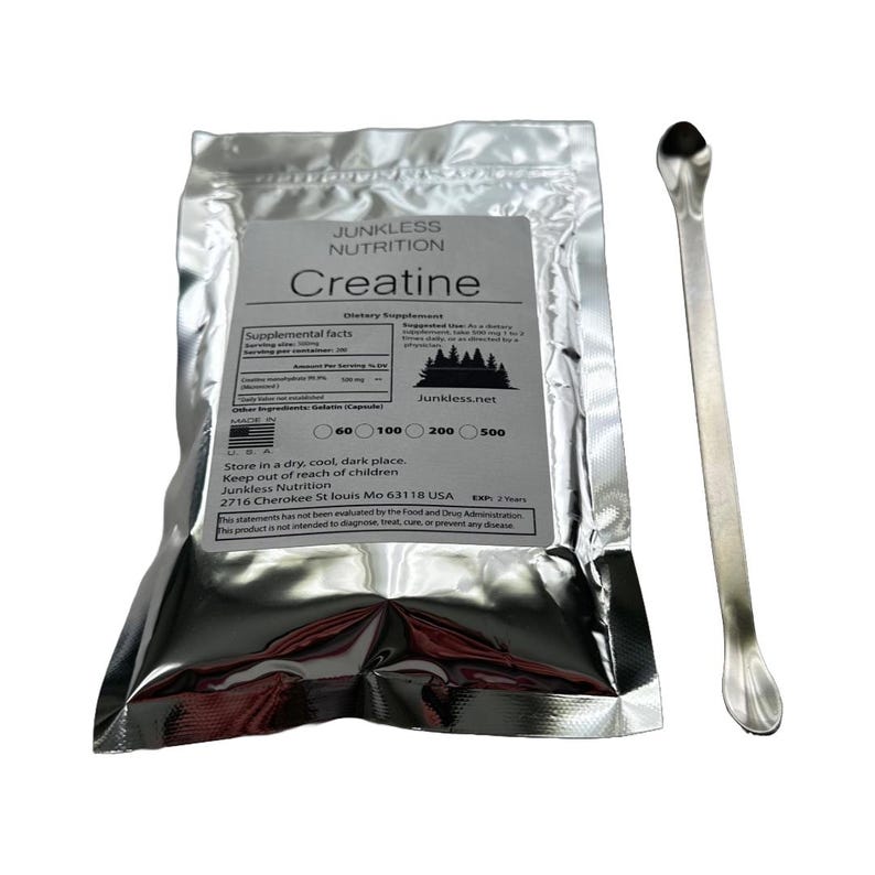 Puede incluir: Un sobre de papel de aluminio plateado de suplemento diet&eacute;tico "Creatina" con una cuchara plateada. El sobre tiene una etiqueta blanca con texto negro, incluyendo informaci&oacute;n nutricional y el logotipo de Junkless Nutrition.
