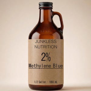 Może przedstawiać: Brązowy szklany dzban z czarną zakrętką i uchwytem. Etykieta głosi "Junkless Nutrition 2% Methylene Blue". Dzban jest oznaczony jako 1/2 Galona, co odpowiada 1893 ml.