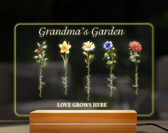 May include: A wooden sign with a clear acrylic insert featuring a floral design. The sign reads "Grandma's Garden" and has the names of five flowers: "Nigel", "Ratil", "Antowan", "Gladys", and "Bianca". The sign also reads "Love Grows Here".