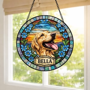 May include: Round stained glass window art featuring a golden retriever with its tongue out. The dog is surrounded by blue flowers and a colorful landscape. The name "BELLA" is displayed on a banner below the dog.