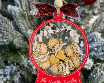 May include: Red and gold Christmas ornament shaped like a snow globe with the text "The Smiths family" at the bottom. Inside the globe are gold hearts and small figures with names like "Dad", "Cedar", "Tyler", "David", "Jessica", and "Will".