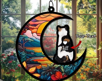 Può includere: Un acchiappasole in vetro colorato a forma di luna con una scena di tramonto colorata e una silhouette di gatto. Il gatto è seduto sulla luna crescente e ha un cuore con il nome "Jill" sul petto. Il testo "Your Text" è visibile nell'angolo in alto a destra dell'immagine.