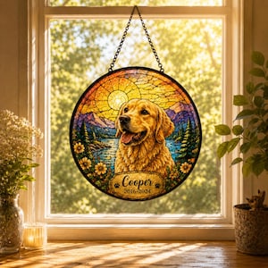 May include: A round stained glass window hanging from a chain. The image features a golden retriever dog with a lake and mountain scene. The text "Cooper 2016-2024" is displayed on a banner at the bottom. The window is framed by a black border.