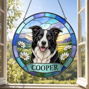 May include: A round stained glass window featuring a black and white Border Collie dog with the name "COOPER" below. The dog is set against a landscape of green fields, white daisies, and a blue sky.