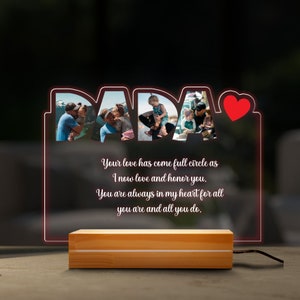 May include: A wooden base with a clear acrylic plaque that lights up. The plaque features the word "DADA" with photos of a family inside each letter. The plaque also includes the text "Your love has come full circle as I now love and honor you. You are always in my heart for all you are and all you do."
