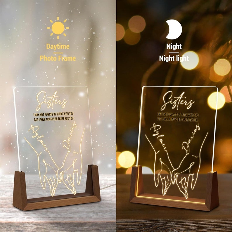 May include: A wooden photo frame with a clear acrylic insert. The insert features a gold outline of two hands holding each other with the text "Sisters" and the quote "I may not always be there with you, but I will always be there for you". The frame can be used as a night light.
