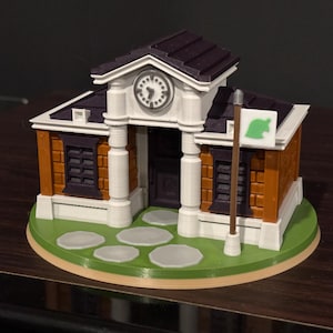 Puede incluir: Modelo impreso en 3D de un edificio con una torre de reloj, paredes de ladrillo y una bandera verde. El modelo presenta una base verde con piedras y un techo marrón. El edificio tiene una fachada blanca y una puerta oscura.