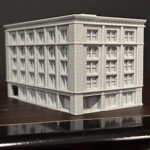 May include: A detailed, gray miniature building with multiple stories and numerous windows. The model features architectural details like arched windows and decorative trim, suggesting a classic or historical design. The building is likely a collectible or a piece for a model train set.