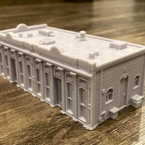 Pu&ograve; includere: Un modello di edificio grigio stampato in 3D con un tetto piatto e pi&ugrave; finestre. L'edificio ha una facciata in mattoni e una piccola porta sul lato.