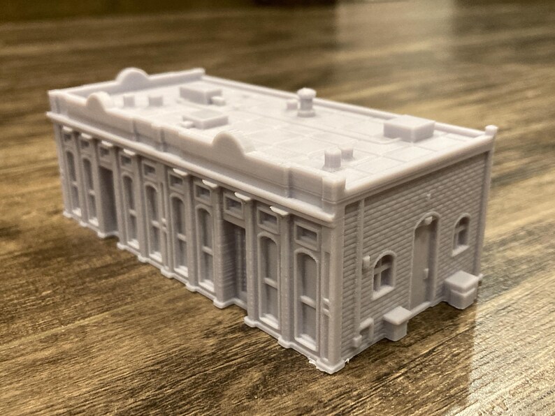 Pu&ograve; includere: Un modello di edificio grigio stampato in 3D con un tetto piatto e pi&ugrave; finestre. L'edificio ha una facciata in mattoni e una piccola porta sul lato.