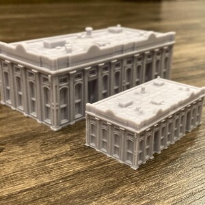 Pu&ograve; includere: Due edifici in miniatura grigi e dettagliati con tetto piatto e colonne. L'edificio pi&ugrave; grande &egrave; sullo sfondo e quello pi&ugrave; piccolo in primo piano.