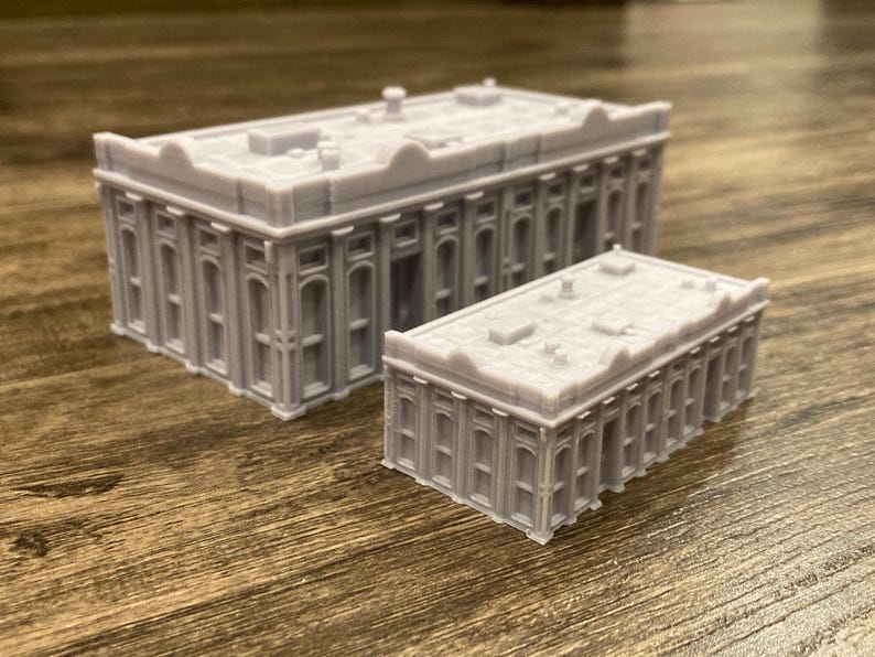 Pu&ograve; includere: Due edifici in miniatura grigi e dettagliati con tetto piatto e colonne. L'edificio pi&ugrave; grande &egrave; sullo sfondo e quello pi&ugrave; piccolo in primo piano.