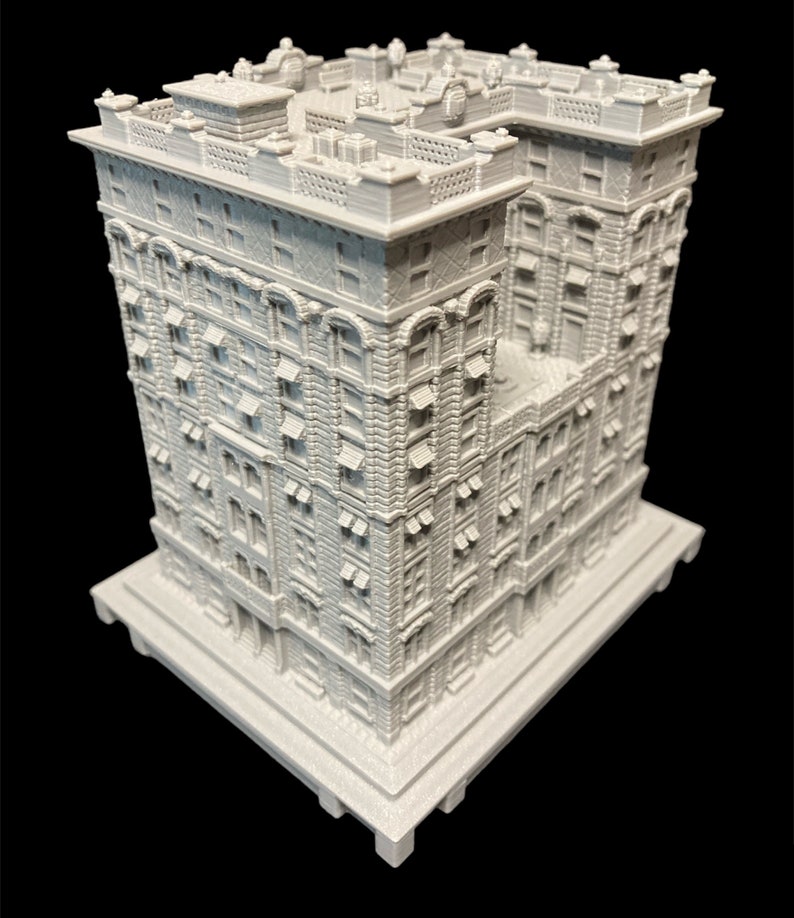 K&ouml;nnte beinhalten: Ein wei&szlig;es 3D-gedrucktes Modell eines hohen, schmalen Geb&auml;udes mit vielen Fenstern und komplizierten Details. Das Geb&auml;ude hat einen quadratischen Sockel und ein flaches Dach.