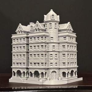 May include: A detailed, gray miniature building with multiple stories, windows, and a central tower. The model features architectural details like arched entryways and a domed roof, suggesting a historic or classical design. The building is set against a dark background.