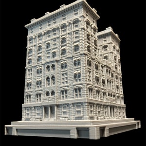 K&ouml;nnte beinhalten: Ein detailliertes 3D-gedrucktes Modell eines grauen Backsteingeb&auml;udes mit mehreren Fenstern und einem kleinen Balkon. Das Geb&auml;ude steht auf einem Sockel und scheint ein Miniaturmodell zu sein.