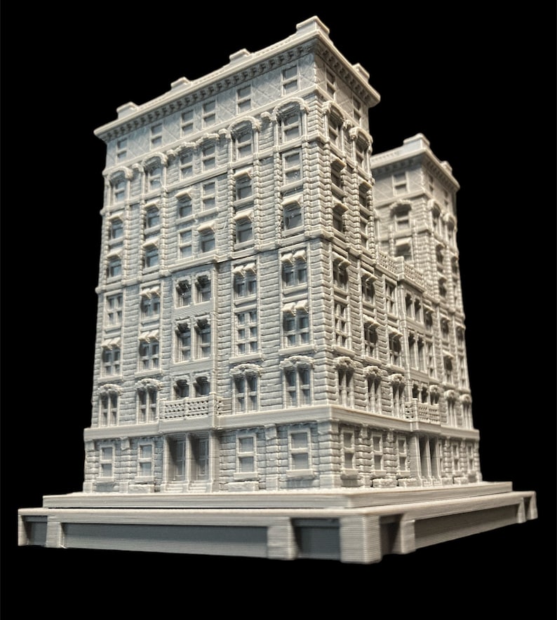 K&ouml;nnte beinhalten: Ein detailliertes 3D-gedrucktes Modell eines grauen Backsteingeb&auml;udes mit mehreren Fenstern und einem kleinen Balkon. Das Geb&auml;ude steht auf einem Sockel und scheint ein Miniaturmodell zu sein.