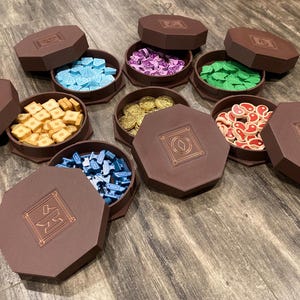 May include: Eight octagonal wooden boxes with lids, each containing different colored game pieces. The boxes are arranged in a circle on a wooden surface.