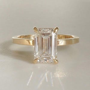 May include: A gold engagement ring featuring a large, clear emerald-cut diamond.