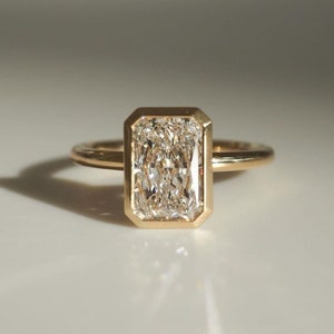 May include: A gold ring with a large, rectangular, clear diamond set in a bezel setting.