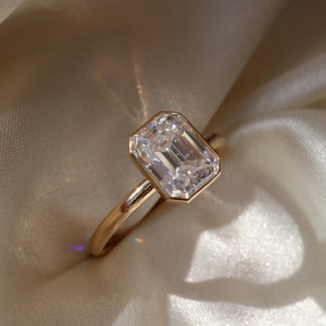 May include: A gold ring featuring a large, clear emerald-cut diamond.