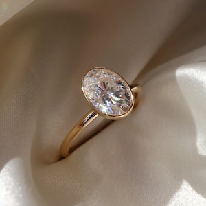 Może przedstawiać: Złoty pierścionek z dużym diamentem o owalnym kształcie.