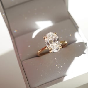 May include: A gold engagement ring with a large oval-shaped diamond in a white box.
